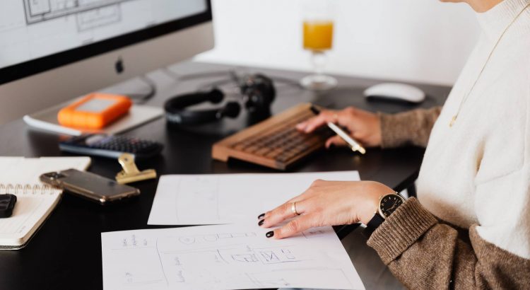 crop anonymous woman working with documents sitting at table with computer